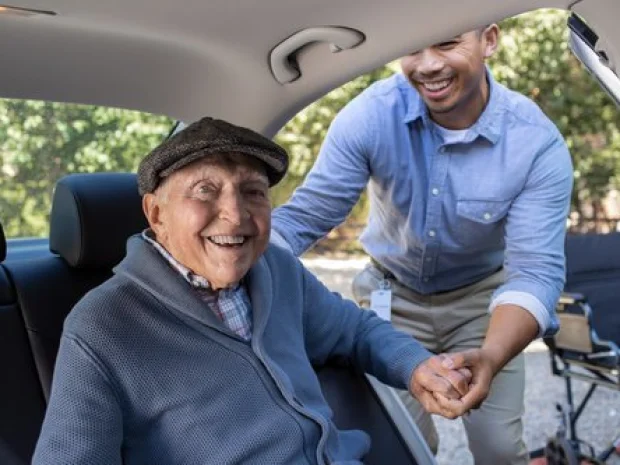 A smiling senior man being helped out of a car by a caregiver